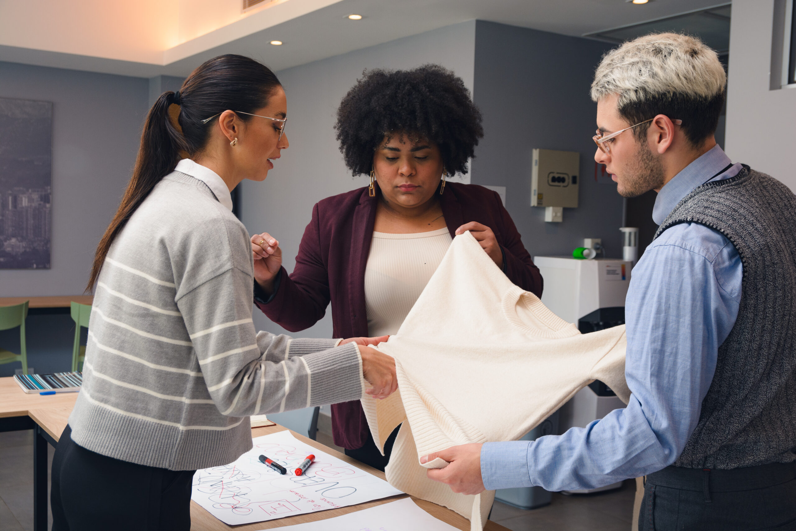 Woman Designer is Evaluating the quality of the fabric and the design of a sweater with her team. She is touching the fabric and is giving clear instructions while her team listens to her attentively