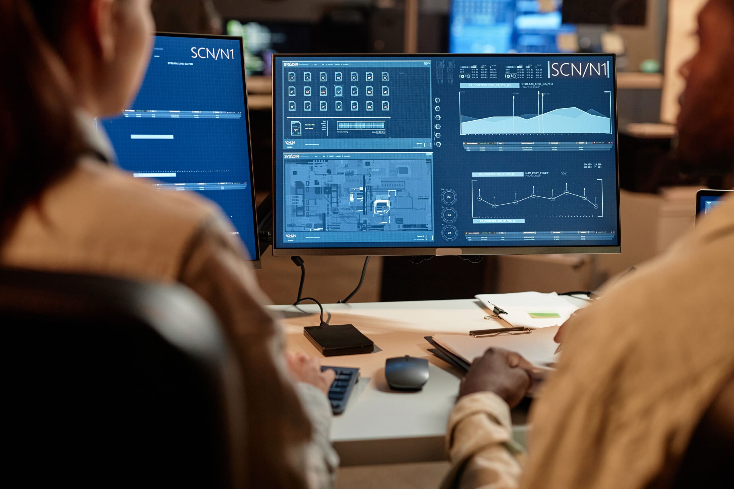 Back view closeup of two data scientists looking at computer screen with charts in office
